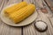 Two ears of boiled corn in a plate and coarse salt on the table. Healthy diet. Fitness diet. For a sweet treat