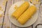 Two ears of boiled corn in a plate, corn kernels and coarse salt on the table. Healthy diet. Fitness diet. For a sweet treat