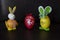 Two easter rabbit figure made of plastic egg, dark background. Green-white and and orange checkered pattern ribbon bow, Yellow-ora