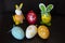 Two easter rabbit figure made of plastic egg, and  four colorful red, yellow, white easter eggs before dark background.