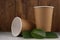 Two eco-friendly cardboard cups with green leaves lie on a concrete surface on a wooden background.Mock-up. Close-up.