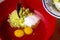 Two egg yolks with white yellow sugar oil and lemon peel in a red bowl for cake preparation