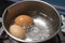 Two eggs in boiling water in stainless steel pan on the kitchen stove