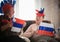 Two elderly enthusiastic women watching TV in russian accessories holding russian flags