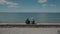 Two elderly individuals seated on a wall overlooking a tranquil sea.