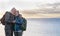 Two elderly people hug each other in front of the winter sea enjoying the sunset light. Standing on the cliff with backpack on his