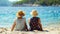 Two Elderly women in straw hats sitting together on seaside sand, summer travel concept