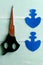 Two elements in the shape of an anchor cut from blue felt. Scissors on wooden background. Step. Closeup. Top view