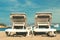 Two empty deckchairs on a sandy beach facing the ocean, blue skies and a small speed boat