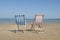 Two empty linen beach chairs one blue and one red in the middle of the image on the beach, facin