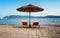 Two empty sun beds deck chairs under umbrellas on an empty sandy beach with sea views