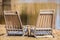 Two empty wooden beach chairs pulled together for conversation in sand beside water with reflections and glare - Selective focus