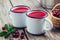 Two enameled mugs of cranberry juice or morsel. A cranberry drinks, basket of berries and pan.