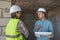 two engineers, a man and a woman in white helmets and protective vests, are standing in the room and holding a plan of