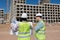 two engineers, a man and a woman in white helmets and protective vests, work at the construction site.