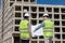 two engineers, a man and a woman in white helmets and protective vests, work at the construction site.