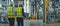 Two engineers in protective helmets and yellow vests walk through the production room