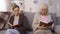 Two envious old women reading books sitting on hall of nursing home, rivalry