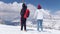 Two excited young women walking on the snow in Dolomites with big backpack and guitar and waving hands