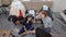 Two exhausted women are sitting on floor in front of couch with sorted clothes from wardrobe, resting