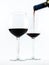 Two exquisite transparent glasses with red wine and a bottle pouring wine on a white background