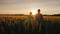 Two farmers, a man and a woman, are looking forward to the sunset over a field of wheat. Teamwork in agribusiness