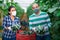 Two farmers in protective mask showcase full boxes of cucumber in greenhouse