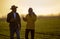 Two farmers walking in field speaking on phone at sunset