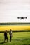 Two farmers watch an agricultural drone fly and fertilize the fields.