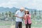 Two farmers wearing hats holding rice plants and observing the yield while standing using tablets