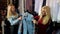 Two fashionable blonde girls choose clothes in a large clothing store.