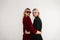 Two fashionable twin sisters with sunglasses in a stylish trendy vintage dress near a gray wall in the studio. Couple young women