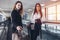 Two female business partners standing on moving walkway with heavy bags going to departure lounge