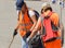 Two female cleaners in orange vests clean outside with tools, outdoor, summer