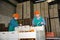 Two female employees of fruit warehouse in colored uniform labeling fresh ripe mandarins in crates