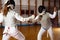 Two female fencers  exercising movements in duel at fencing room