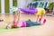 Two female fitness models doing yoga exercises, one lying on floor mat holding legs of another above her in a sports