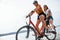 Two female friends on the bike have fun at beach near the lake