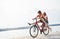 Two female friends on the bike have fun at beach near the lake