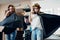 Two female friends goofing around in front of the camera making moustache from hair and curler standing in flying cape