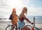 Two female friends riding their bicycles along seaside promenade