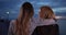 Two female friends share friendly moment together at the pier at dusk