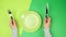 Two female hands hold a metal knife and fork, in the middle, there is an empty round green plate