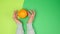 Two female hands jerk a whole ripe orange on a green background