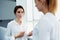 Two female managing directors talking about something personal while standing in hallway of modern office interior,