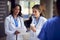 Two Female Medical Staff Wearing White Coats Discussing Patient Notes Meeting In Busy Hospital