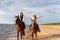 Two female riders leading two majestic horses along a beach coastline.