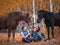 Two female riders sit on the grass next to the horses