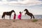 Two female riders in vibrant pink dresses leading two majestic horses along a beach coastline.