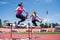 Two female sportswomen are jumping over an obstacle. Running with hurdles. Active lifestyle.